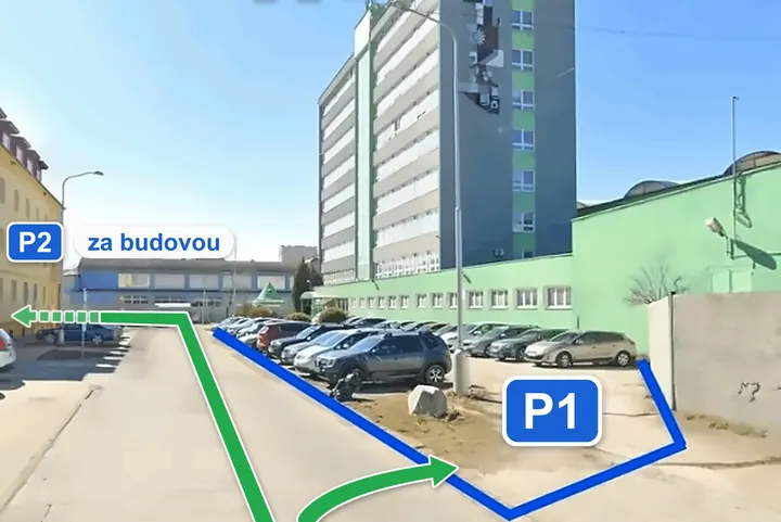 Pohľad z auta na konci Komenského ulice: vpravo parkovisko P1 pred budovou VÝVOJ, šípka rovno a doľava vedie na parkovisko P2 za budovou